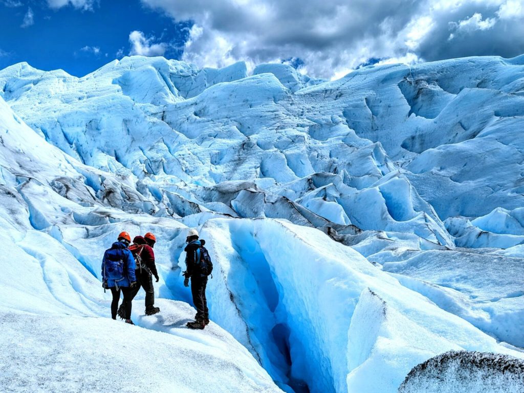 res personas con cascos y mochilas realizando una caminata sobre el hielo azul profundo y blanco del Glaciar Perito Moreno en El Calafate, Santa Cruz.