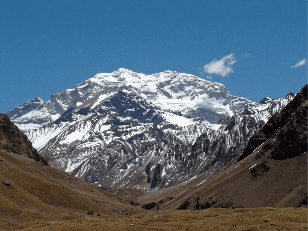 El imponente Cerro Aconcagua con sus picos nevados y glaciares resaltando bajo un cielo azul profundo, visto desde el valle.